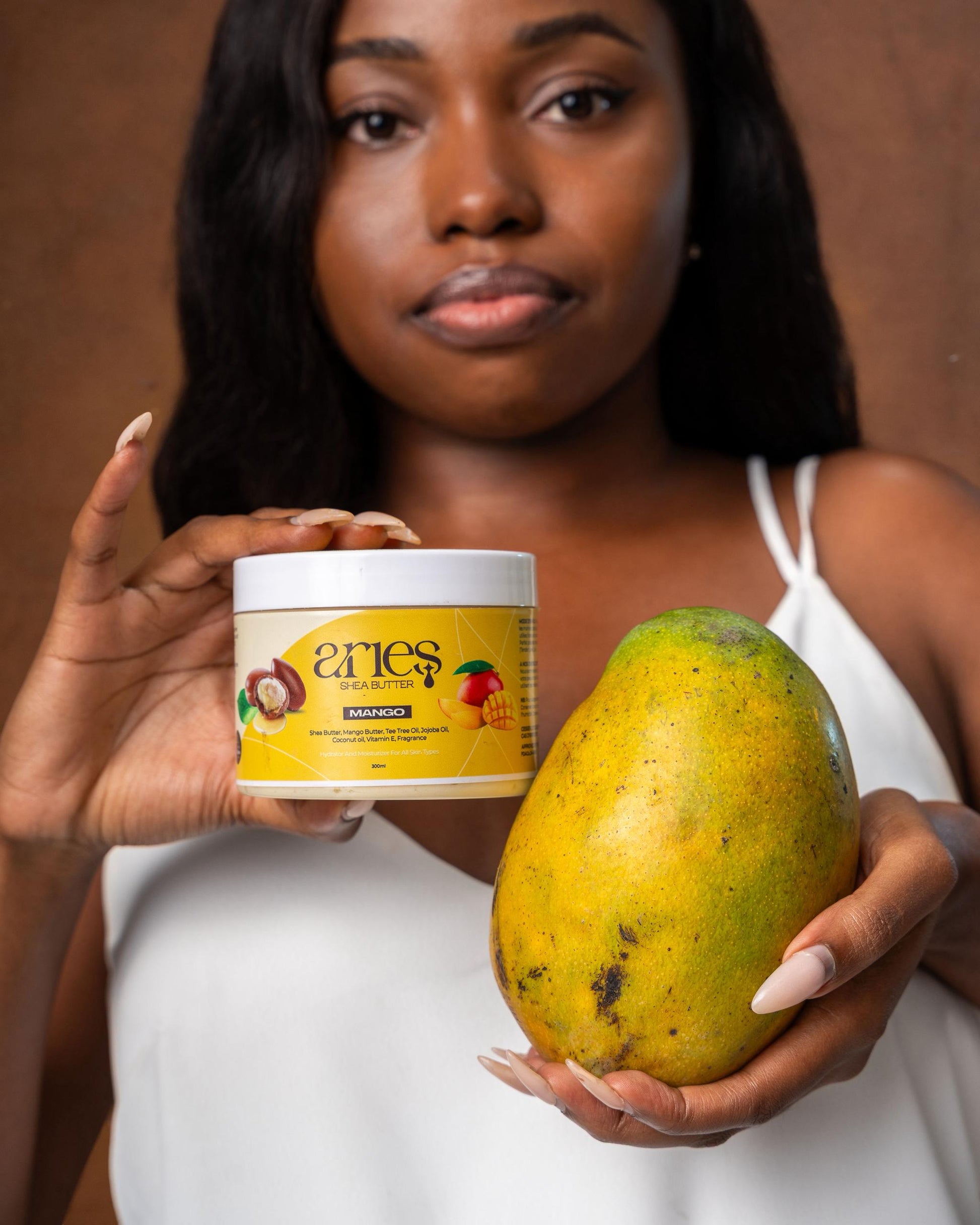 Woman holding a jar of shea product and a mango against a brown background

