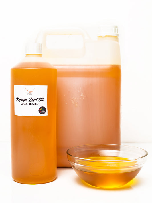 Two bottles of papaya seed oil with a small bowl of oil on a white background